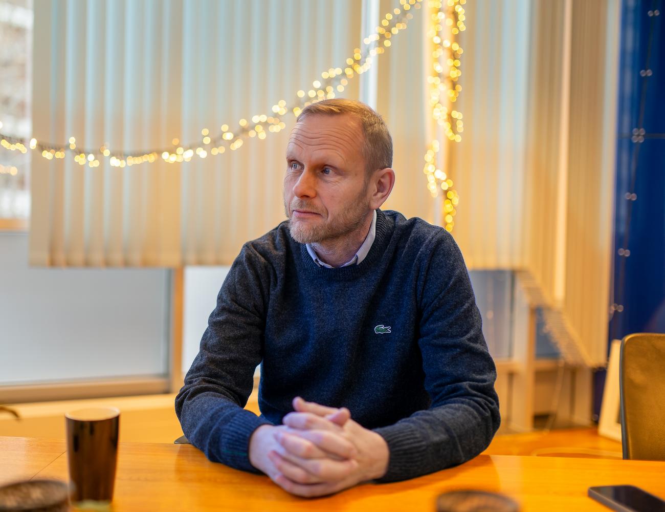 Man i bl&aring; genser sitter ved m&oslash;tebord